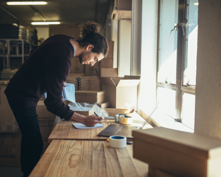 Young man reviewing and packing products in a well-lit warehouse, representing the inventory management and logistics process in an e-commerce, key to improving the conversion rate on a website.