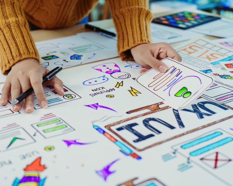 Designer working on a UX/UI project, reviewing and organizing colorful sketches and wireframes on a table.